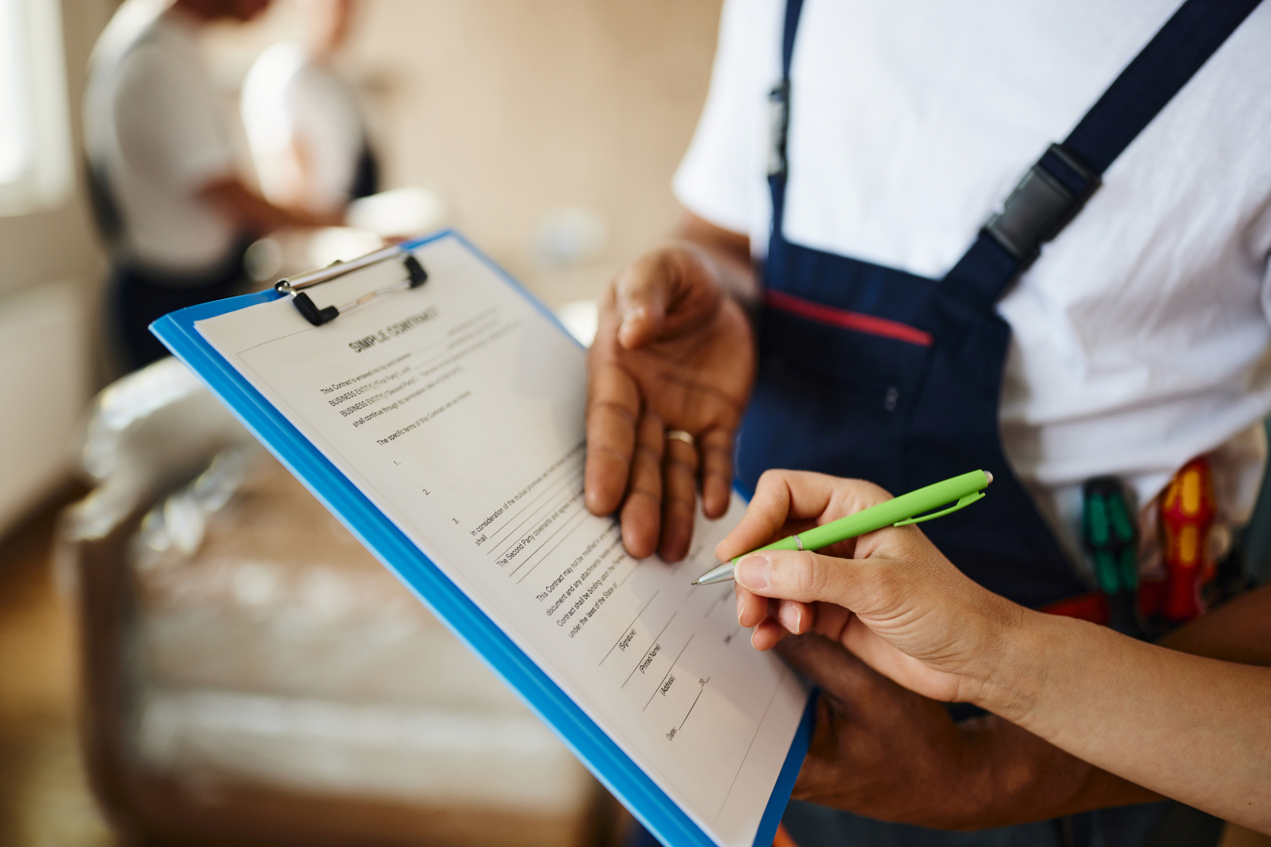 Close up of unrecognizable black mover showing his customer where to sign the receipt for furniture in her new apartment.